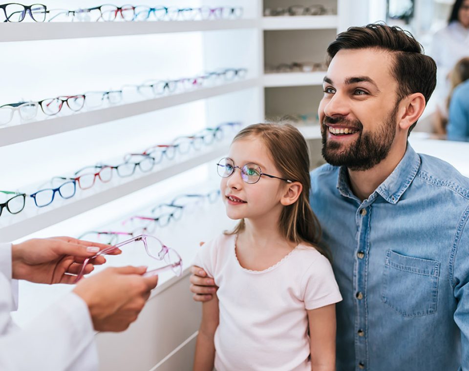 Handsome young man and his little cute daughter are choosing the best apropriate eyeglasses in modern ophthalmology clinic. Dad and daughter with doctor ophthalmologist.