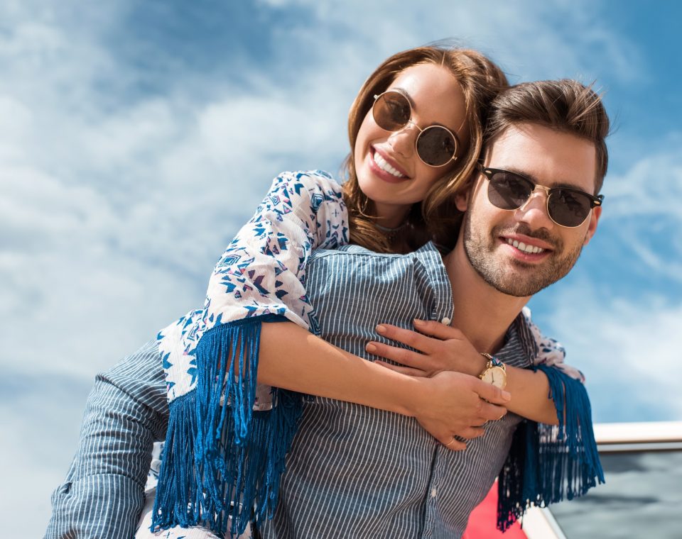handsome man in sunglasses piggybacking his smiling girlfriend